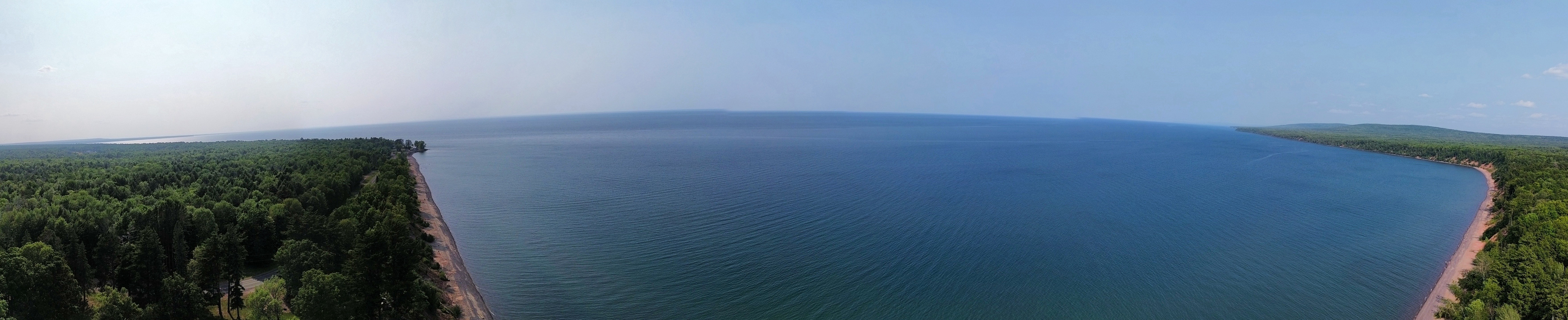 Ultra-wide aerial panorama of a huge blue lake wrapped by forested shoreline