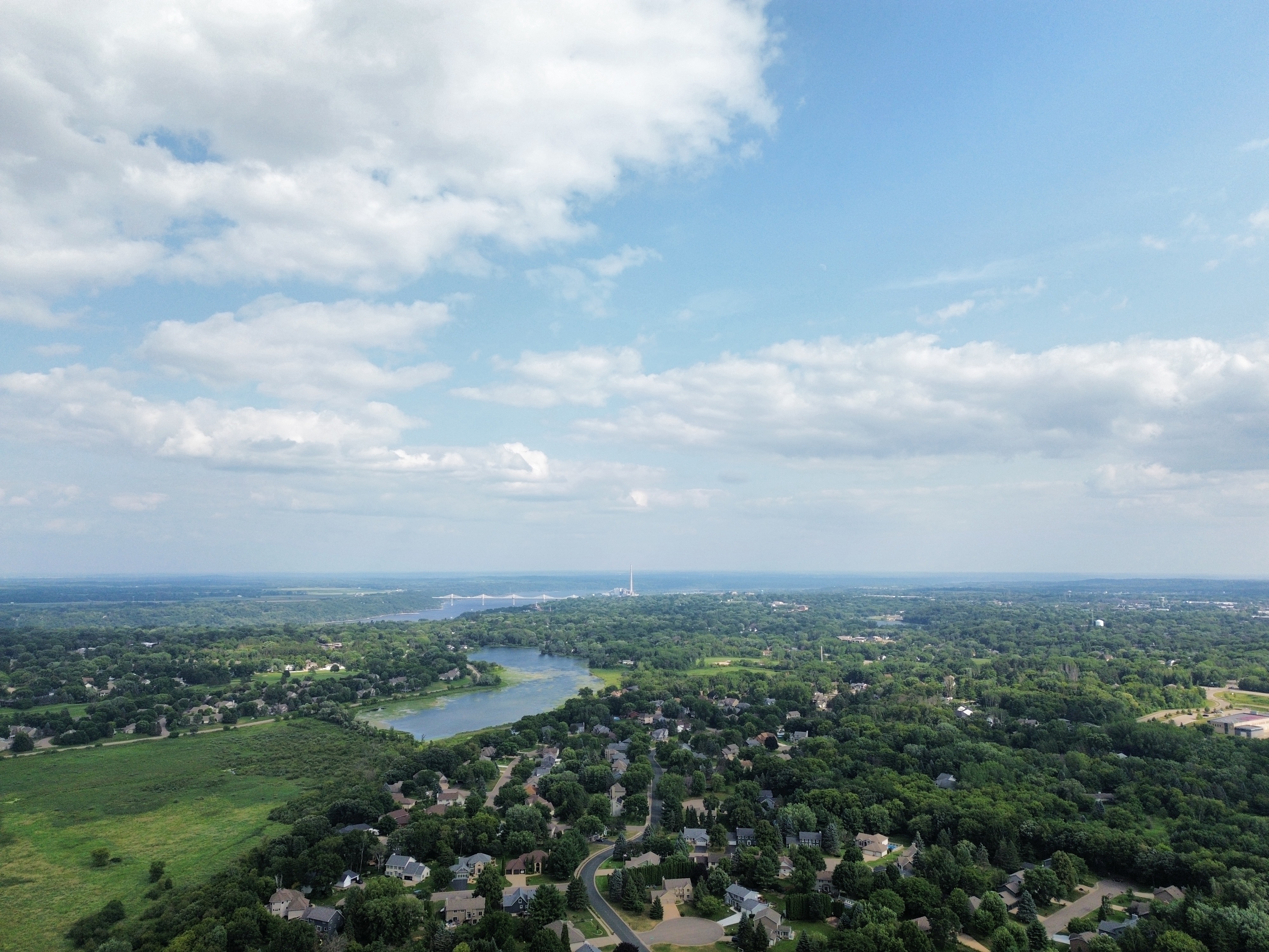 Aerial view of a wooded neighborhood beside a lake with a river and bridge on the horizon