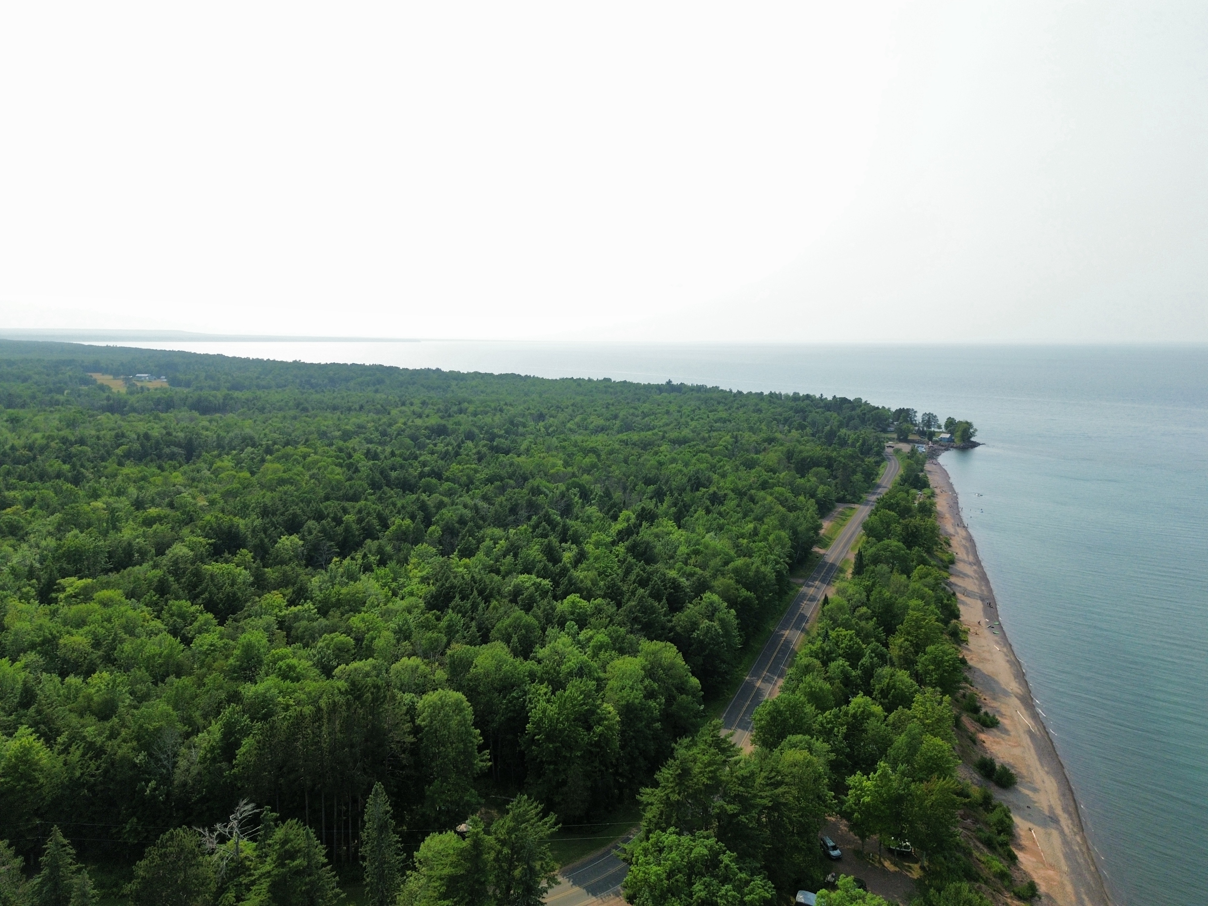Aerial view of a forested shoreline with a highway running beside a long sand beach and open water