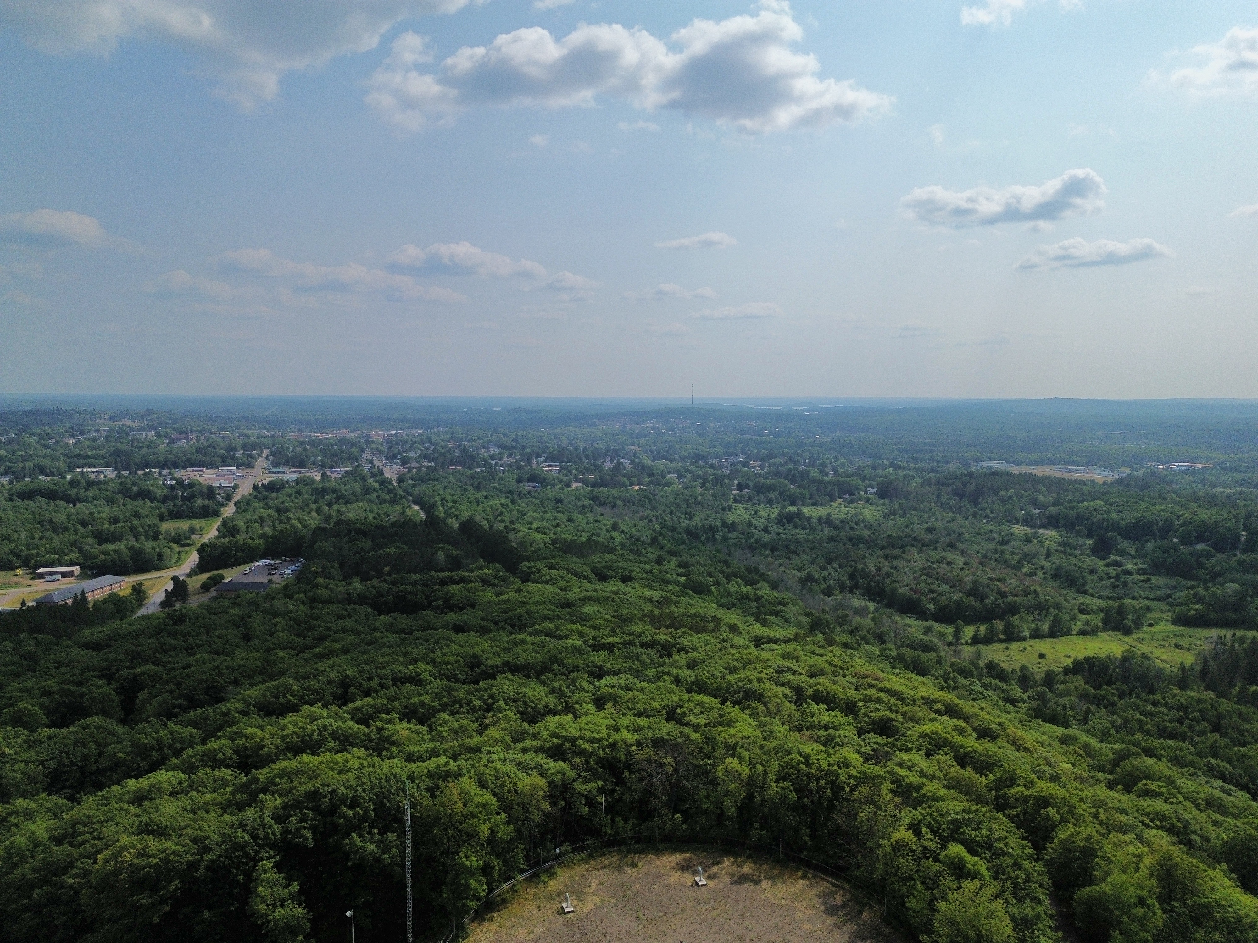 Aerial view over dense green forest ridge looking toward a small town in the distance